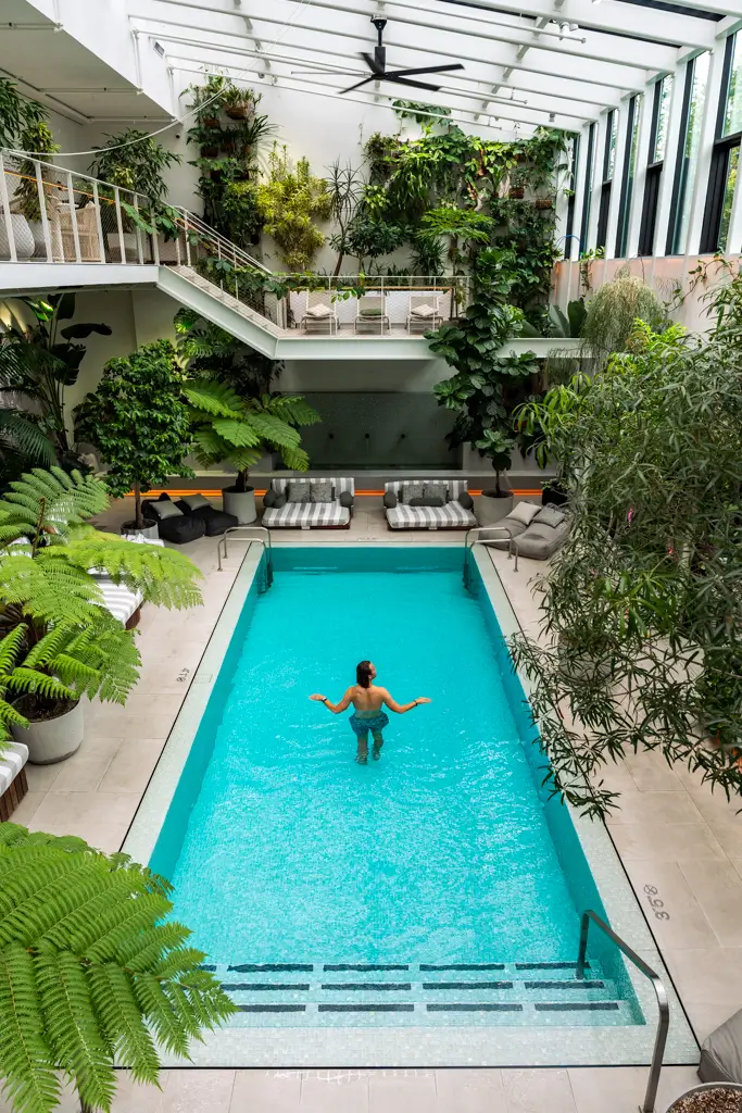 JT Mocarski of The Mobile Homie relaxing in the indoor thermal springs pool at Cascada in Portland, Oregon, surrounded by lush tropical plants and modern lounge seating.