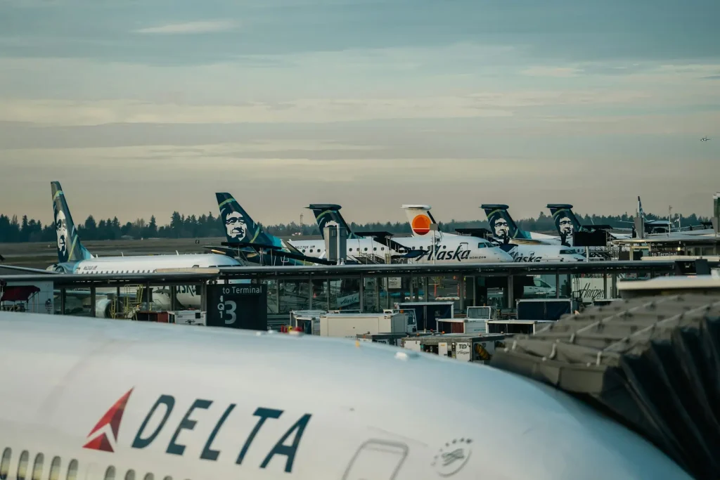 Alaska Airlines and Delta aircraft parked at the gates at Seattle-Tacoma International Airport (SEA) in Washington, with multiple Alaska Airlines planes visible across the terminal.