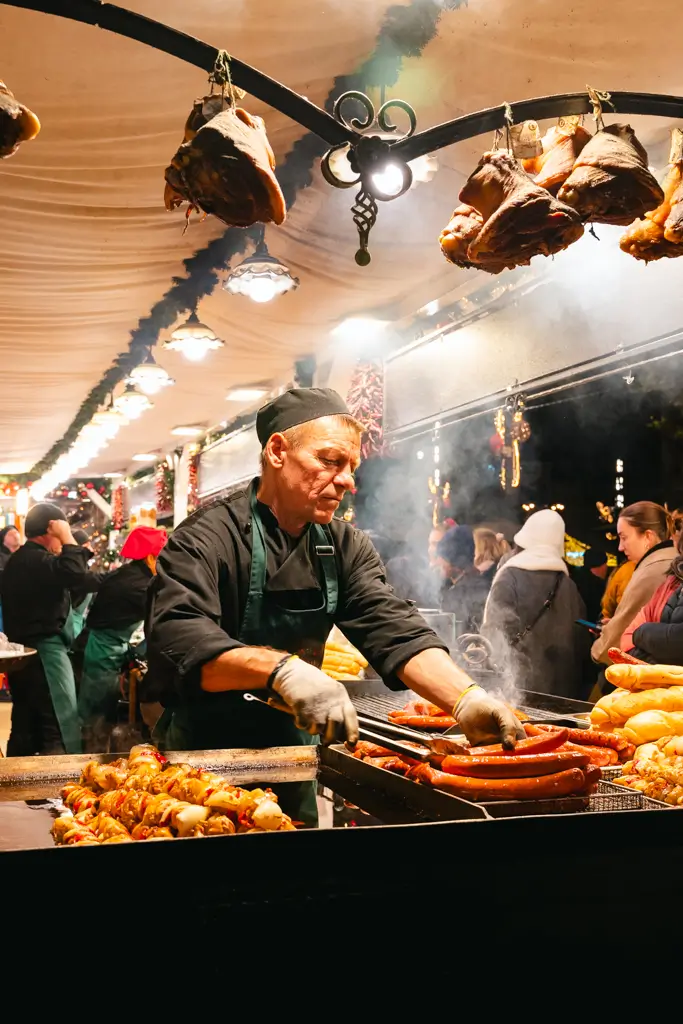 Vendor grilling sausages and other traditional Hungarian foods over a smoky grill at a Christmas market in Budapest, Hungary.