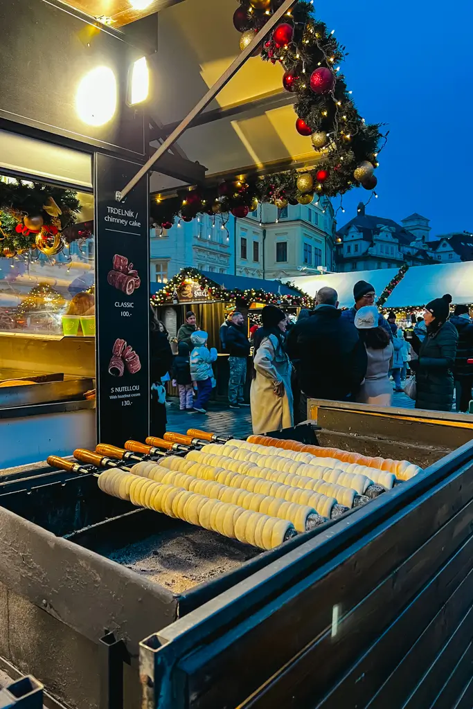 Traditional trdelník chimney cakes cooking on rotating spits at a festive Christmas market in Prague, Czech Republic.