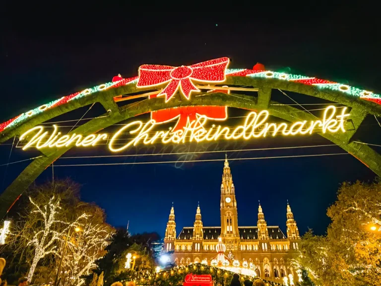 Illuminated entrance to the Vienna Christmas Market at Rathausplatz at night, with festive lights and Vienna City Hall glowing in the background.