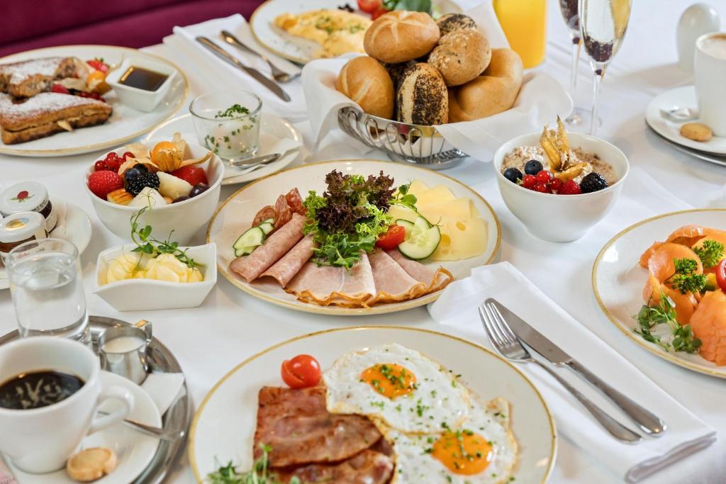 Austrian hotel breakfast spread at Austria Trend Parkhotel Schönbrunn with fried eggs and bacon, a platter of ham and Swiss cheese, smoked salmon, a basket of Kaiser and seeded rolls, fresh berries, French toast, muesli, black coffee, orange juice, and sparkling wine in Vienna, Austria.