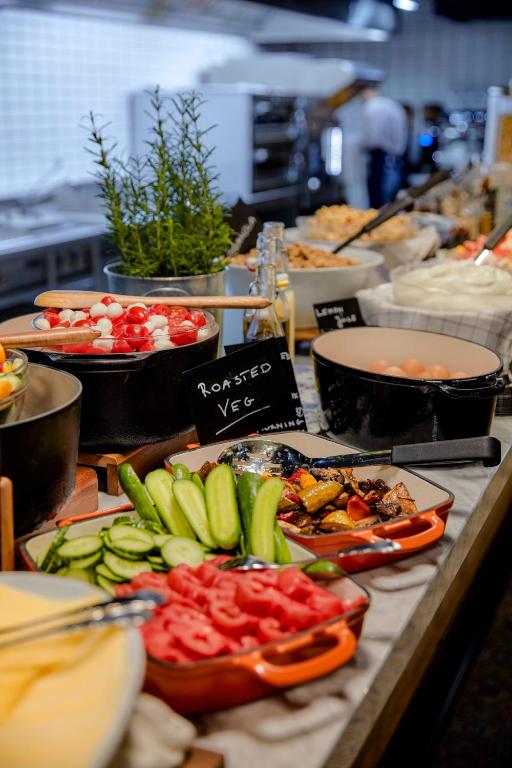Breakfast buffet at Max Brown Hotel 7th District with orange enameled cast-iron dishes of sliced tomatoes, cucumbers, and roasted vegetables, a pot of mozzarella and cherry tomatoes, a pot of hard-boiled eggs, a chalkboard sign reading Roasted Veg, and a rosemary plant in Vienna, Austria.