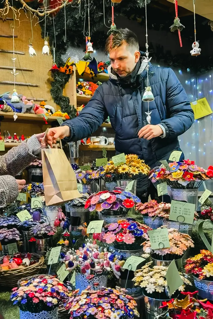Colorful handmade ceramic flowers and ornaments displayed in decorative pots at a Christmas market stall in Budapest, Hungary.