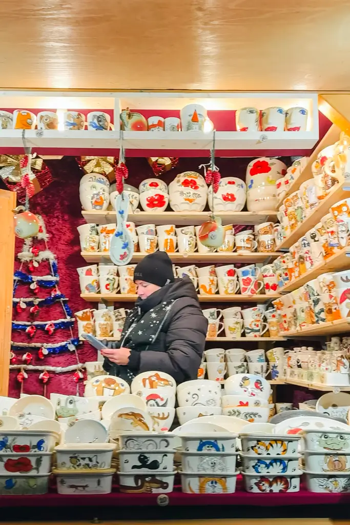 Colorful hand-painted ceramic mugs, bowls, plates, and dishes featuring whimsical animals and floral designs at a European Christmas market.