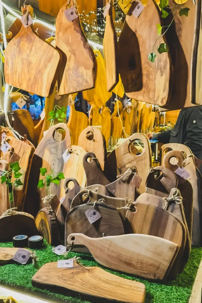 Handcrafted wooden cutting and serving boards in a variety of shapes and natural wood tones displayed at a European Christmas market.