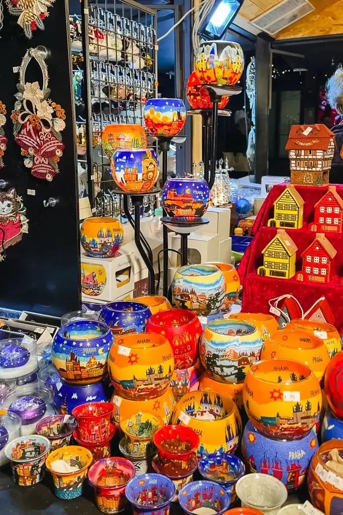 Colorful glass candle holders painted with Prague landmarks and winter scenes displayed at a Christmas market stall in Prague, Czech Republic.