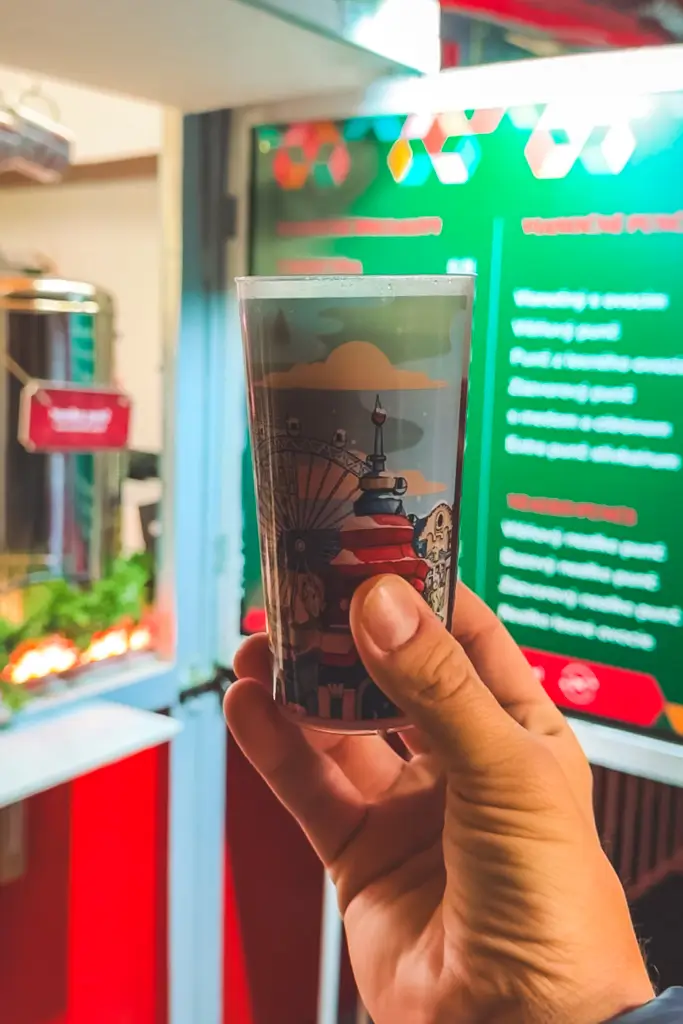 Hand holding a traditional Christmas market drink in a souvenir cup decorated with a festive European city scene.